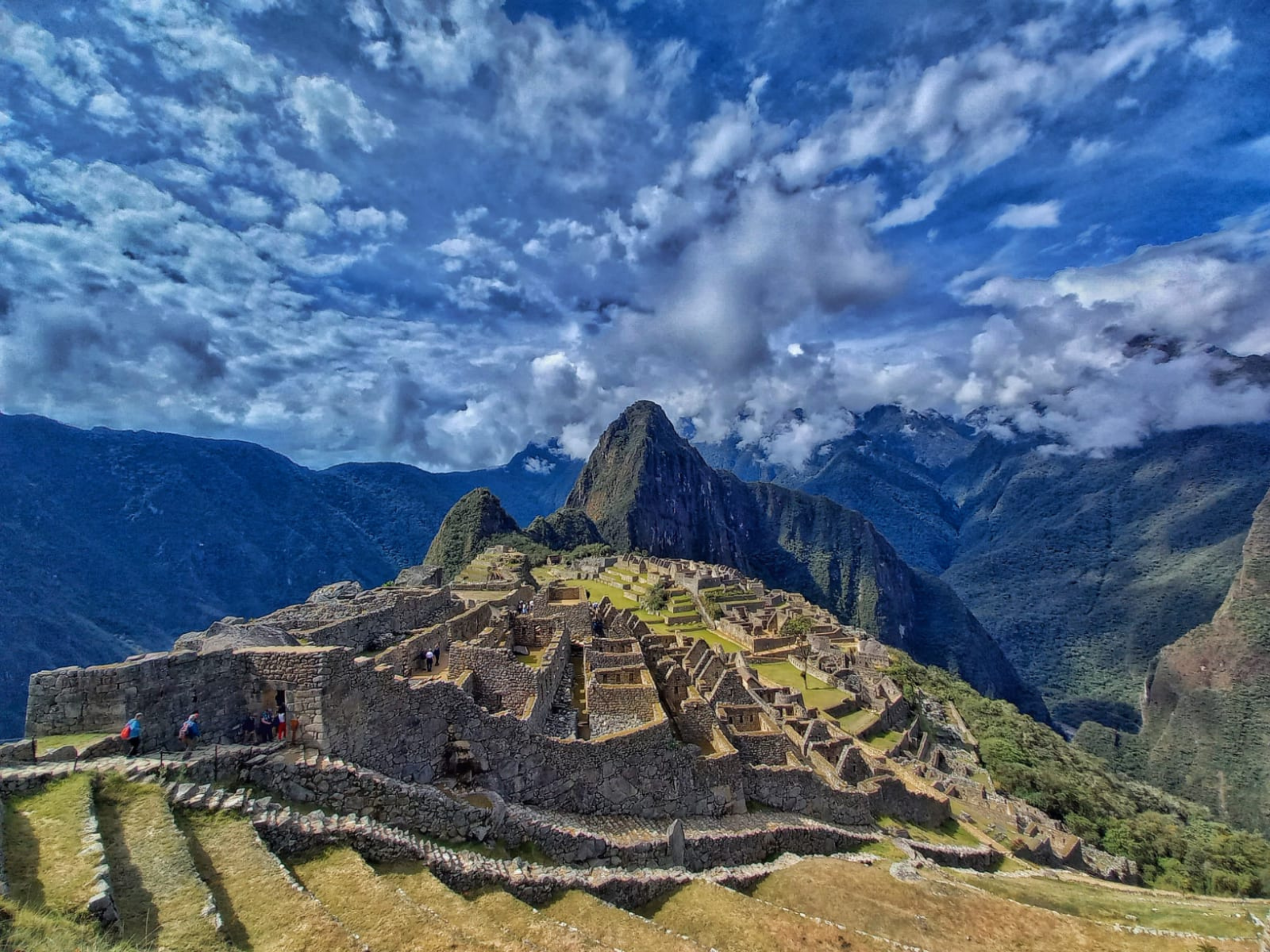 A panoramic view of Machu Picchu in Peru under a partly cloudy blue sky. The ancient Incan ruins are nestled in a lush, mountainous landscape, with highlights including stone structures in the foreground and a prominent peak in the background, offering a perfect setting for a private trip. A panoramic view of Machu Picchu in Peru under a partly cloudy blue sky. The ancient Incan ruins are nestled in a lush, mountainous landscape, with highlights including stone structures in the foreground and a prominent peak in the background, offering a perfect setting for a private trip.