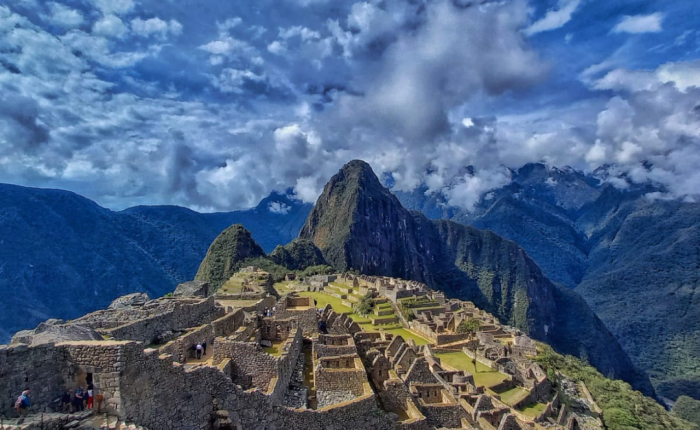 Steep terraces and stone structures of Machu Picchu are highlights seen under a vibrant blue sky filled with scattered clouds, with lush green mountains rising in the background. Experience this wonder on a private trip to Peru.