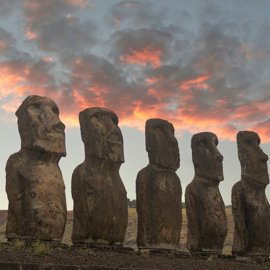 Five Moai statues stand in a row against a vibrant sunset sky with red and orange clouds on Easter Island, inviting you to imagine upcoming adventures beyond the horizon.